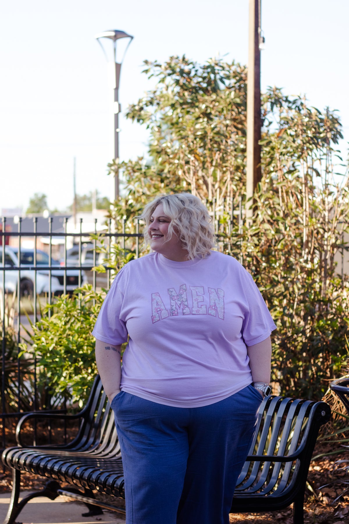 Woman wearing a light purple t-shirt with 'AMEN' printed on it, standing outdoors.