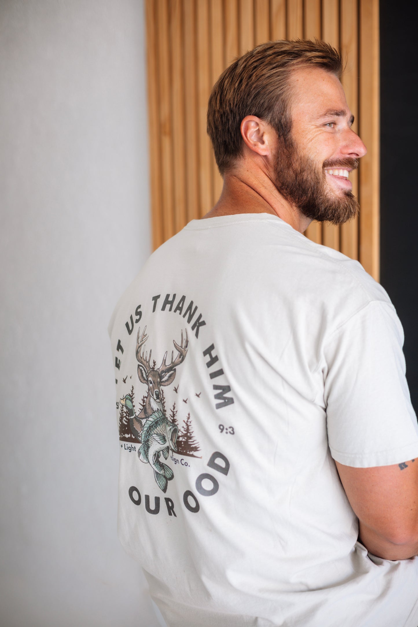Back of a cream Christian T-shirt featuring “Let Us Thank Him for Our Food” Genesis 9:3 with deer, duck, fish, and outdoor graphics.